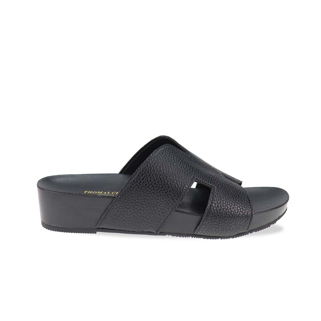 A sleek pair of Thomas Chan's H-Strap Pebble Lychee Flatform Sandals in black displayed in a studio setting, showcasing the pebble lychee-textured H-strap and lightweight flatform sole.