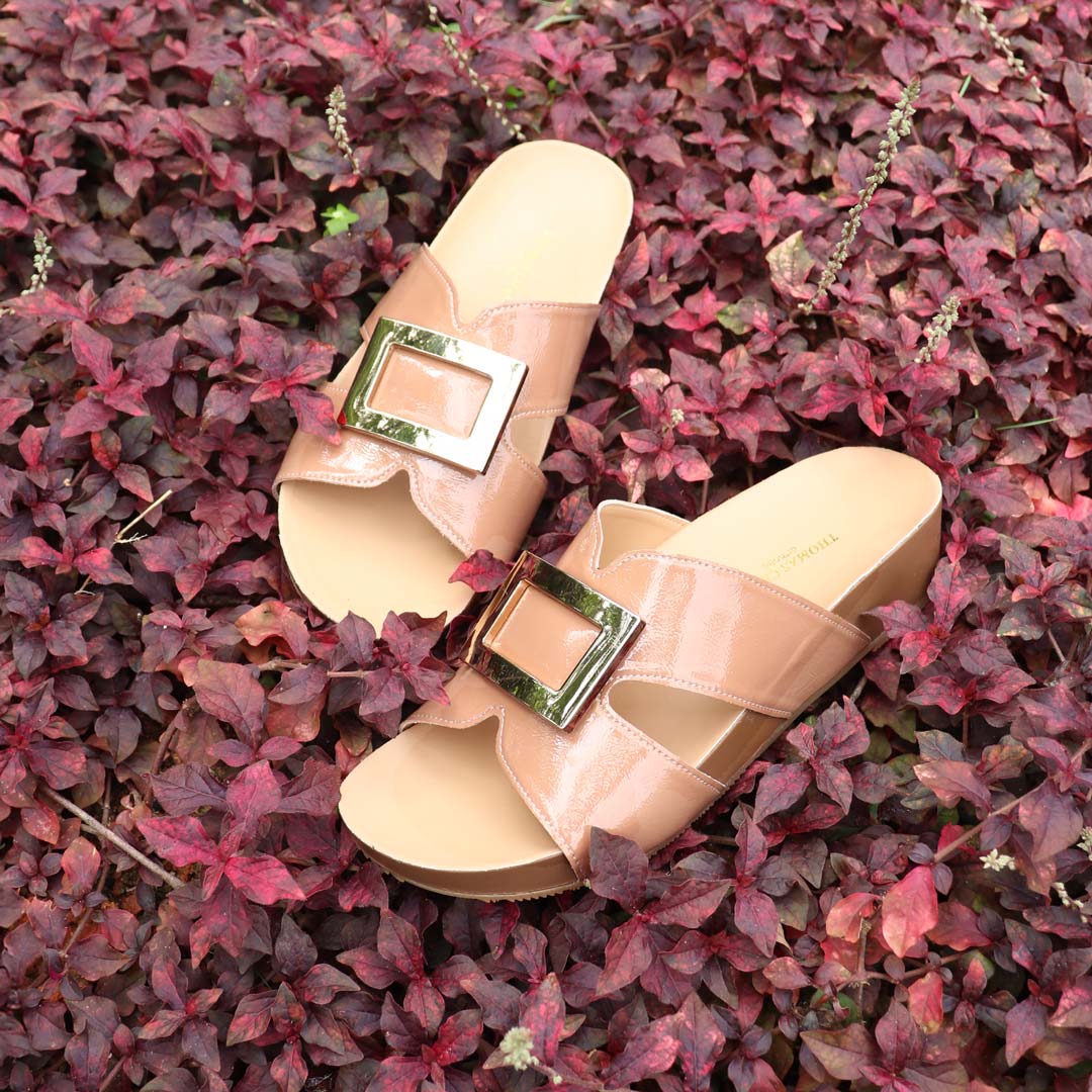 Thomas Chan LiteStep flatform sandals in nude patent leather with square gold buckles, laid on vibrant red foliage background.