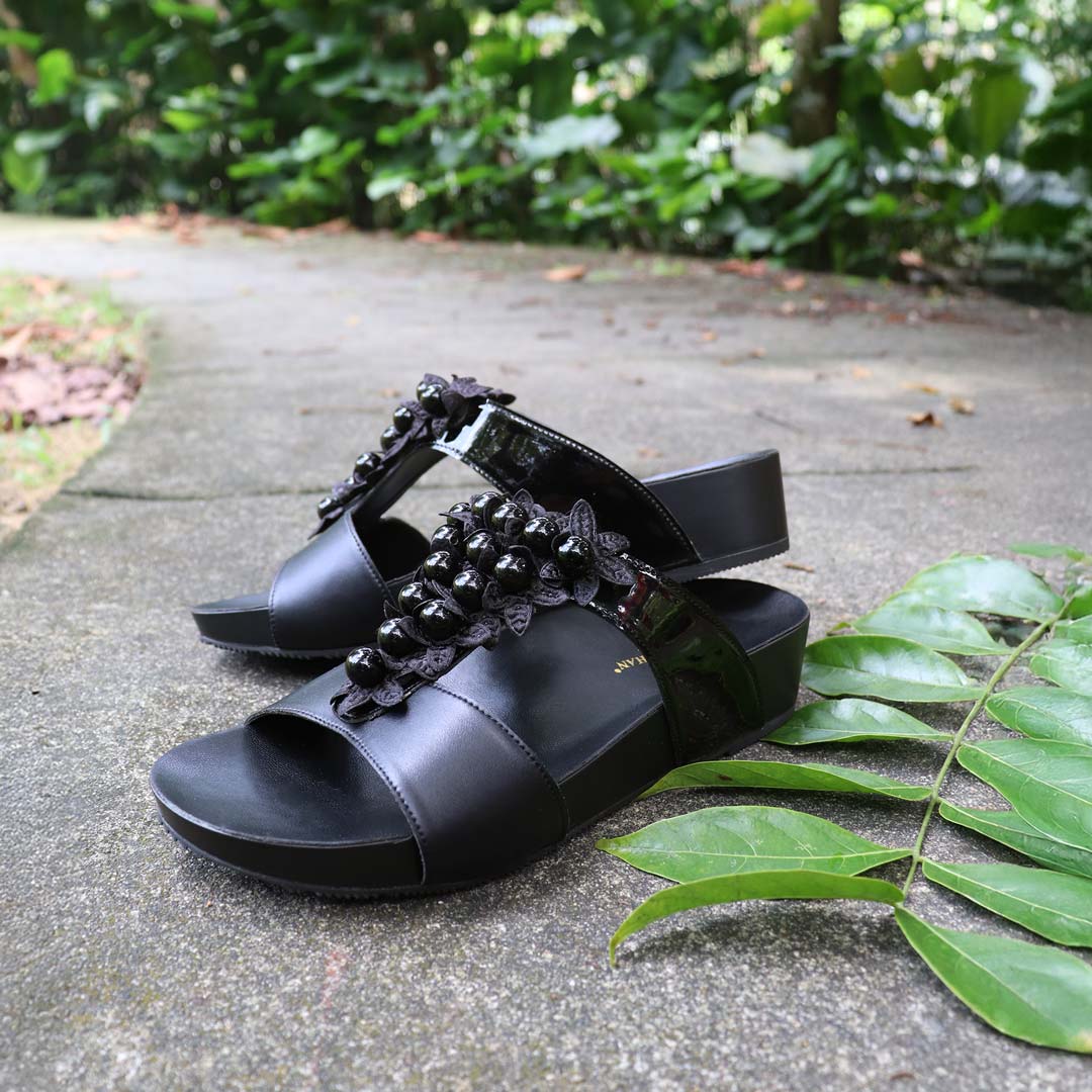 Thomas Chan Petal Pearl Flatform Sandals in black displayed on a textured cement surface with greenery decor—featuring handcrafted petal-inspired pearls and LiteStep cushioned footbed.
