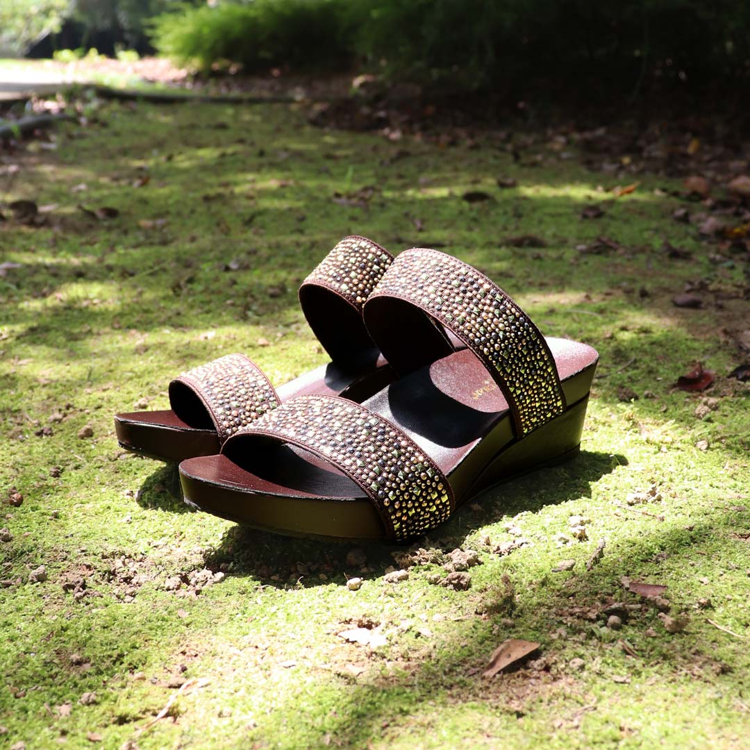 Blinkies Twin Band Wedges by Thomas Chan โ rhinestone low wedge sandals for women in brown, photographed in natural sunlight on mossy garden ground.