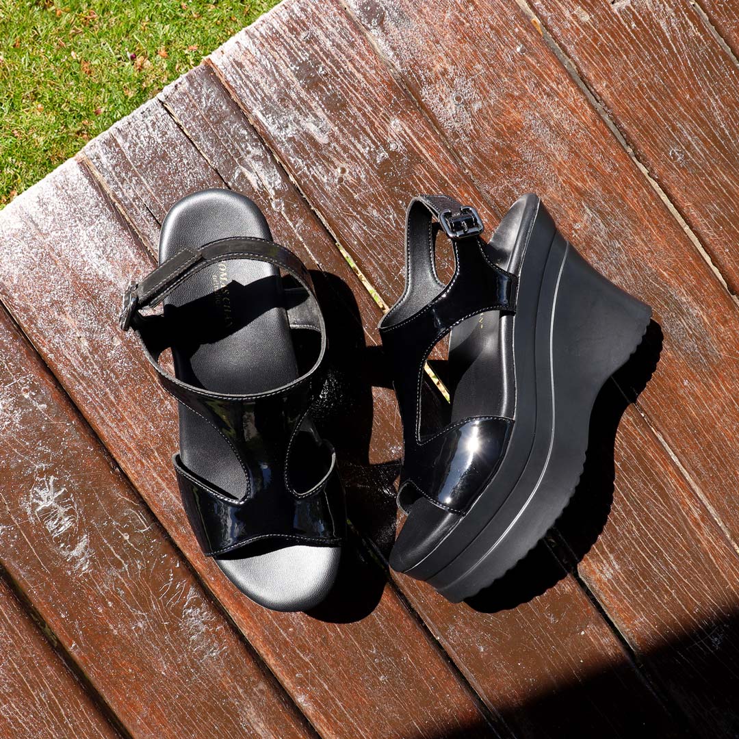 The heels displayed on a wooden floor in an outdoor pavilion, illuminated by natural light, highlighting their elegant contrast against the rustic texture.