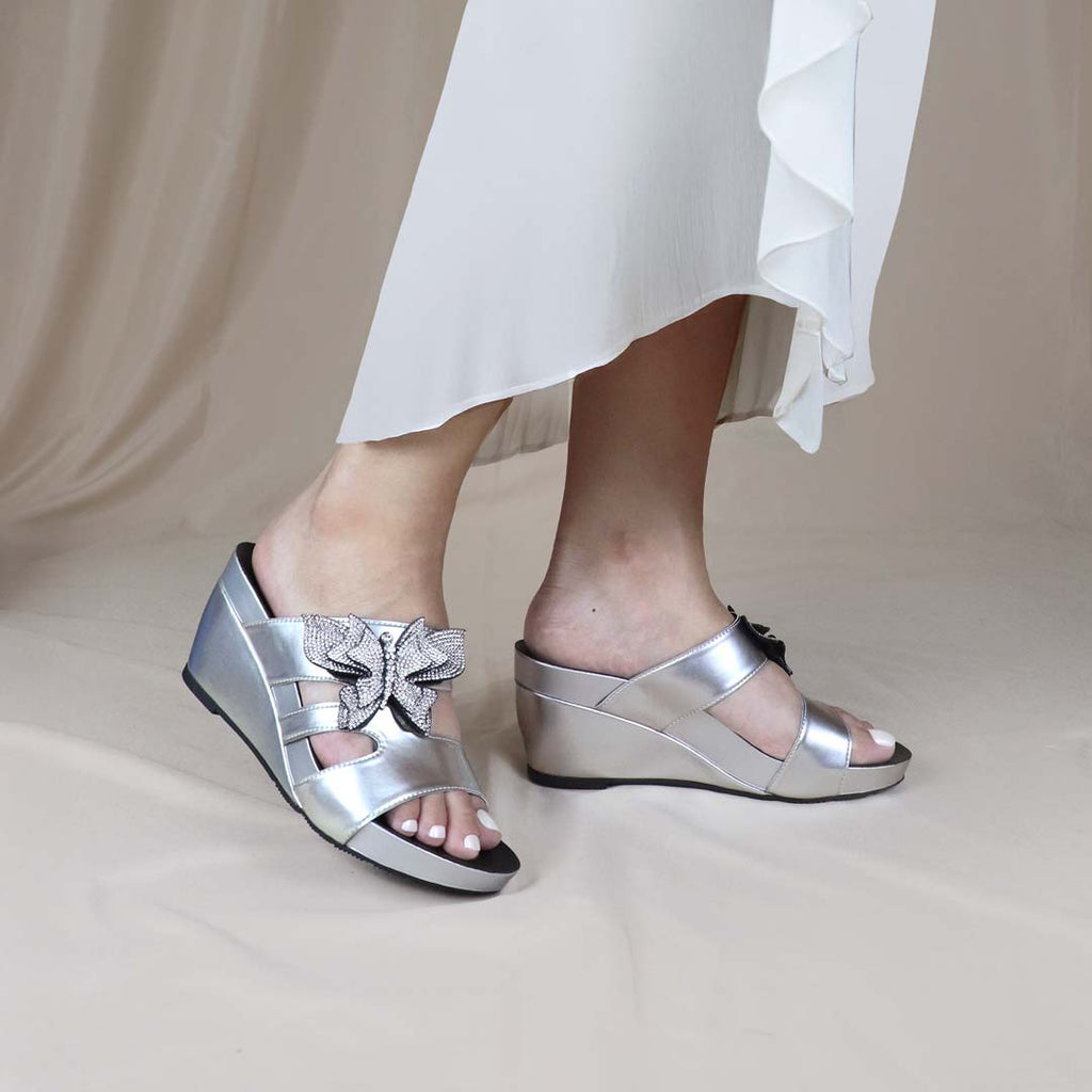 Model wearing Thomas Chan’s Glimmer Butterfly Dinner Wedges with a white dress against a cream backdrop, highlighting the elegant silhouette and sparkling butterfly detail for a refined dinner look.