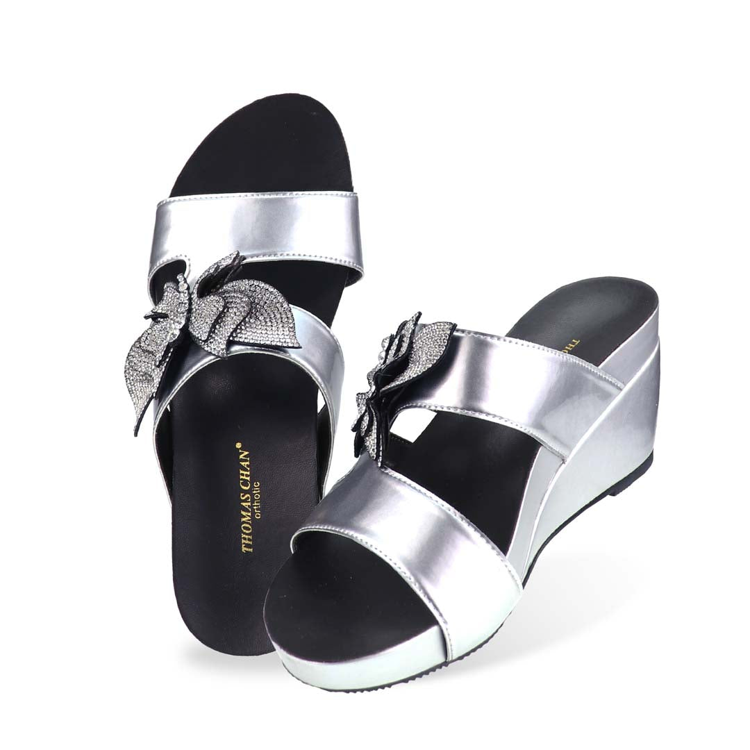 Studio top-down view of Thomas Chan’s Glimmer Butterfly Dinner Wedges, displaying the twin straps, soft inner footbed, and statement butterfly ornament at the center.