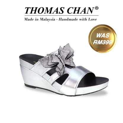 Thomas Chan’s Glimmer Butterfly Dinner Wedges in a diagonal studio view, showcasing the metallic silver finish, rhinestone butterfly detail, and 3-inch ArchLegance wedge. The Orthotic Arch-legance footbed ensures both style and comfort."THOMAS CHAN®" brand displayed with "Made in Malaysia · Handmade with Love" below. Gold and white banner highlights special offer: "Was RM399".