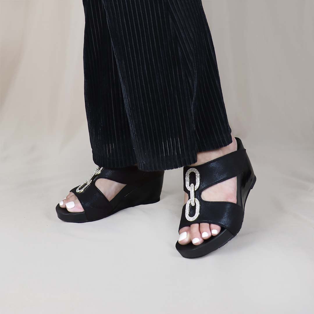 Model standing indoors in Aurora Chain High Wedges by Thomas Chan, featuring glitter fabric, diamond chain accents, and supportive arch design.