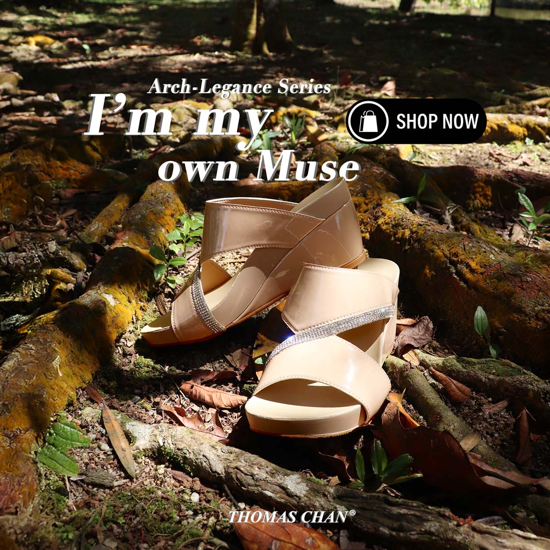 The Thomas Chan Diamond Strap Dinner Wedges rest elegantly on a bed of yellow mossy tree roots, seamlessly blending nature with luxury. The shimmering multi-row diamond straps catch the sunlight, creating a dreamy, ethereal aesthetic perfect for special occasions. Overlaying the image are the words "I’m My Own Muse" and "Arch-Legance Series", with a "Shop Now" button inviting viewers to explore. The Thomas Chan logo is positioned at the bottom, reinforcing the brand’s signature elegance and craftsmanship.