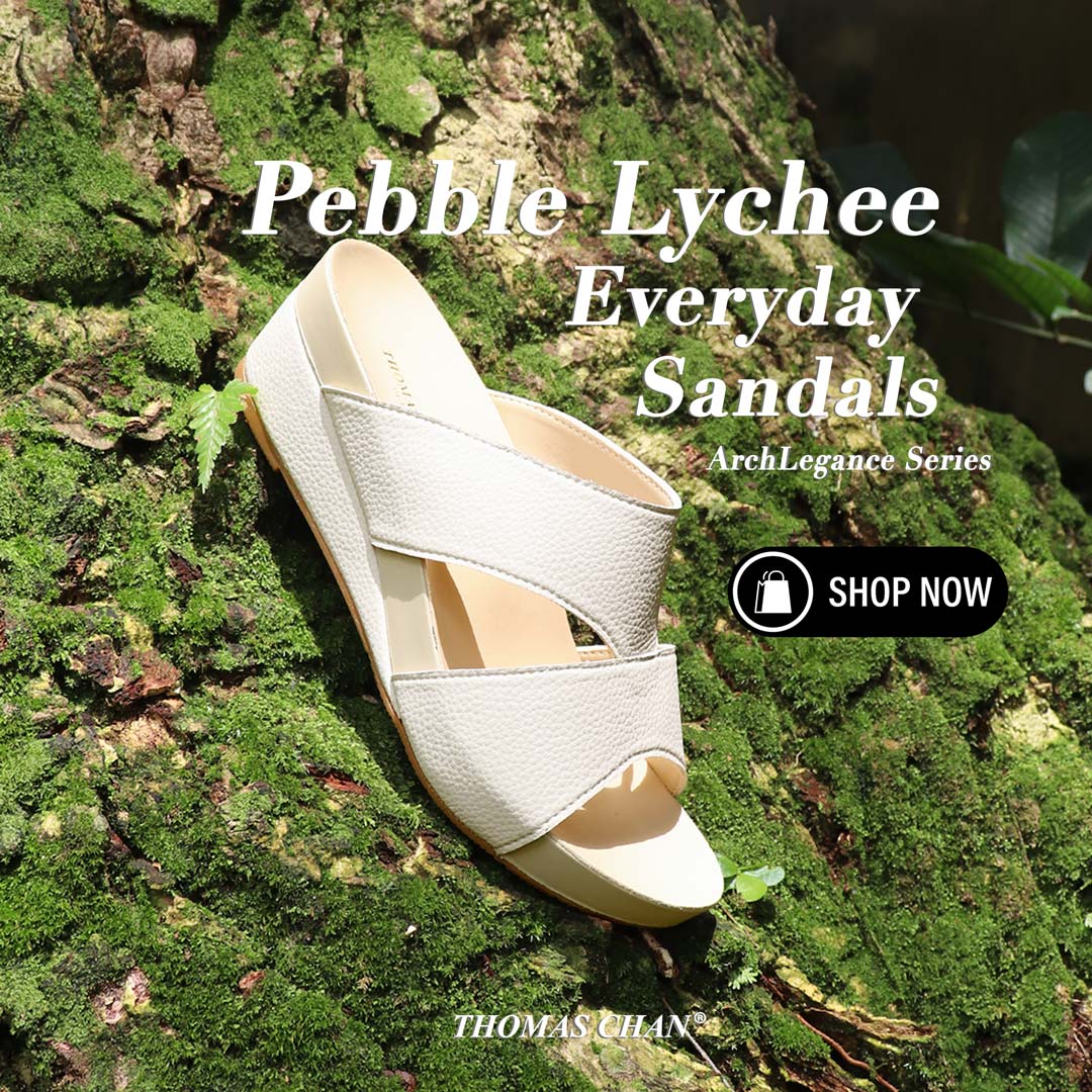 A pair of ivory Pebble Lychee Everyday Sandals from the Thomas Chan ArchLegance Collection, placed elegantly on a moss-covered tree trunk. The sandals feature textured pebbled material and a soft arch-support footbed, blending nature and comfort.