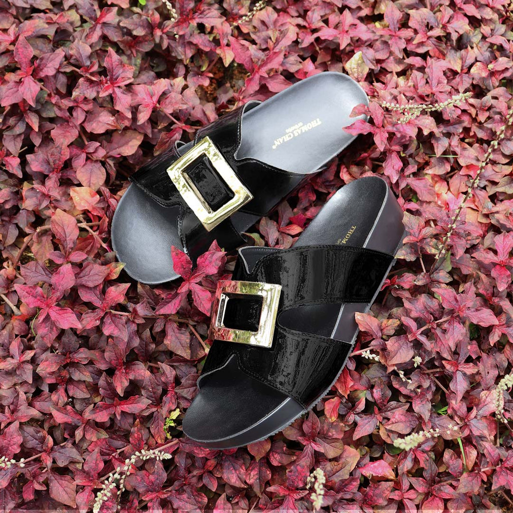Thomas Chan LiteStep flatform sandals in black patent leather with square gold buckles, laid on vibrant red foliage background.