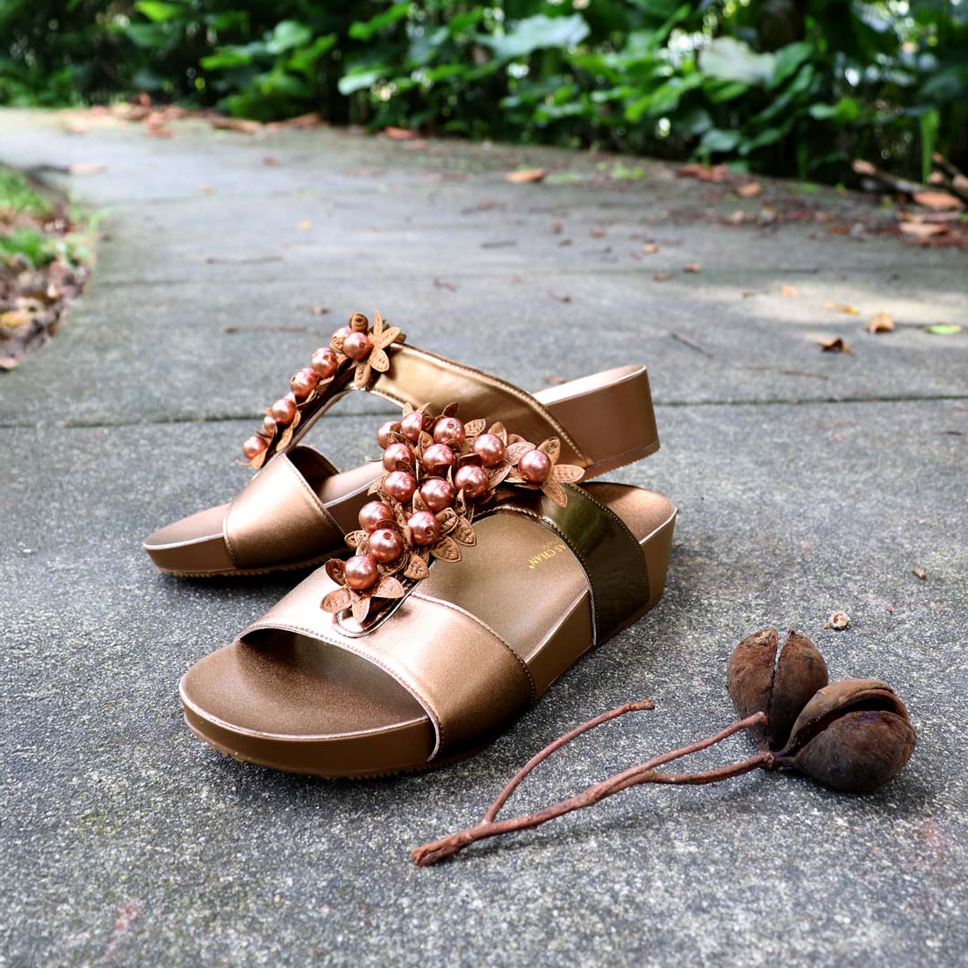 Thomas Chan Petal Pearl Flatform Sandals in bronze displayed on a textured cement surface with greenery decor—featuring handcrafted petal-inspired pearls and LiteStep cushioned footbed.