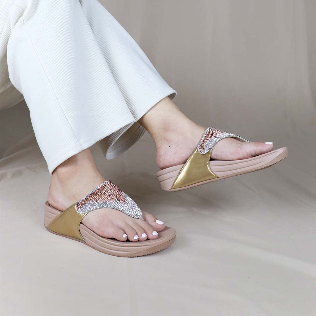 A model sits outdoors wearing the Diamond Embellished Flip-Flop Sandals, with legs crossed and feet slightly lifted. The sandals’ crystal-embellished straps shimmer under natural light, complementing the relaxed and stylish look. The Bounce Care rubber sole ensures a cushioned, comfortable feel while enhancing the overall aesthetic.