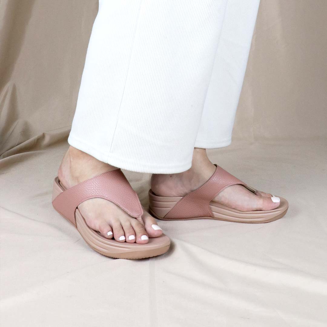Thomas Chan’s pastel-tone pink flip-flop sandals worn by a model in a flowing white dress, posed against a soft cream backdrop—offering a minimalist, elegant lifestyle aesthetic.