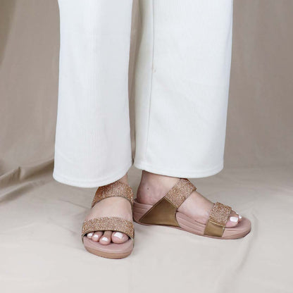 A model standing while wearing the Diamond Embellished Duo-Strap Bounce Care Sandals in Bronze, effortlessly showcasing their stylish yet comfortable design. The soft rubber sole and sparkling embellishments enhance the outfit, blending comfort with elegance.